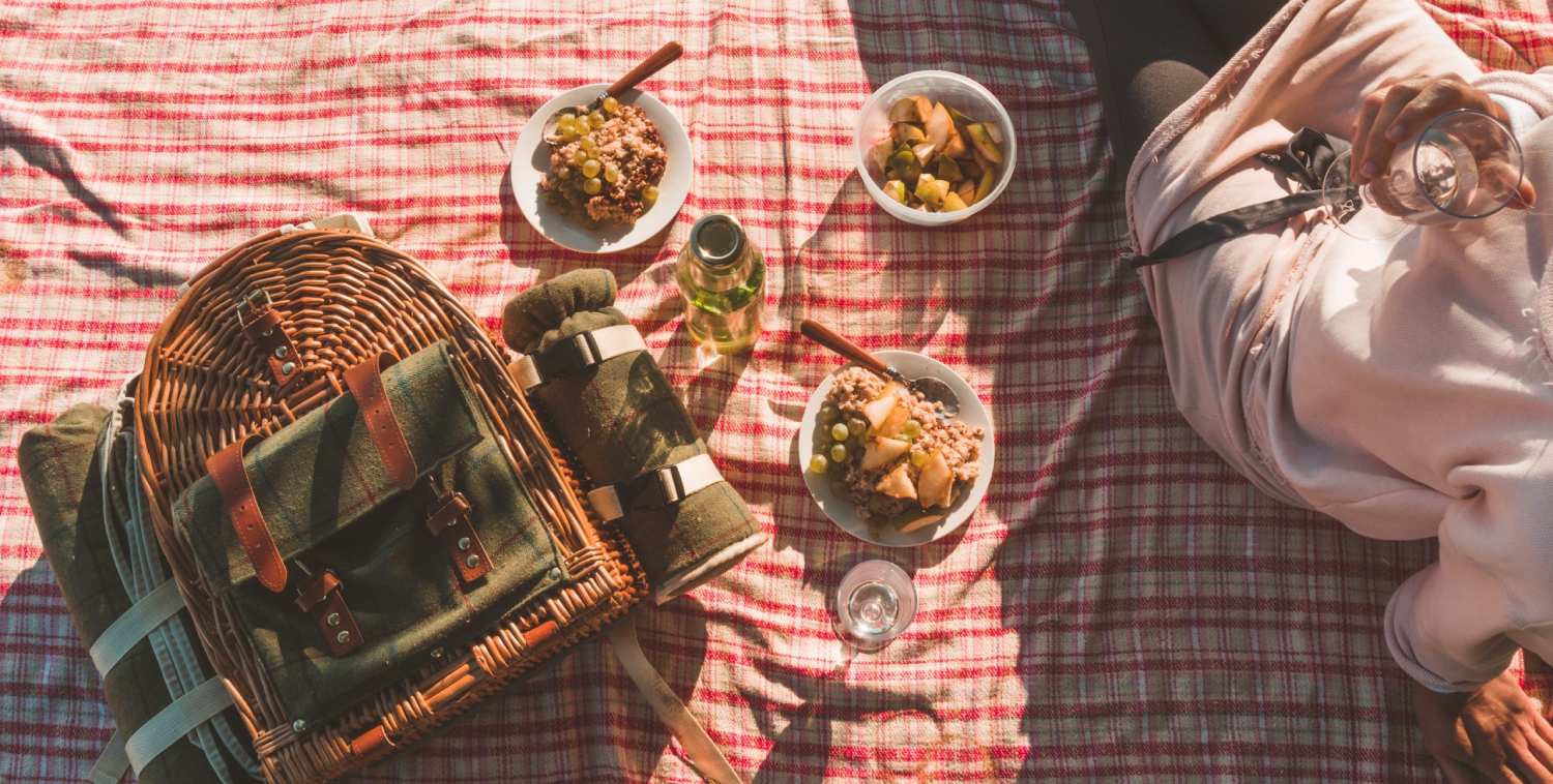 Idyllic picnic setup at Conti di San Bonifacio Wine Resort in Tuscany with a wicker basket, food bowls, and a person relaxing on a checkered blanket.